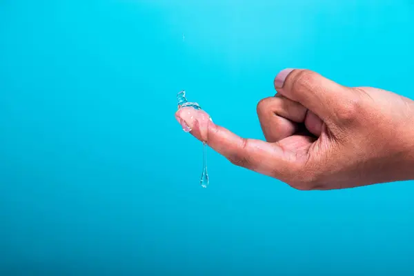 Bir parmakta jel damlası ve açık mavi arkaplan.