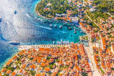 Yaz boyunca hareketli liman ve rıhtım güvertesinin yukarıdan görünüşü demirli tekneler, berrak turkuaz sular ve Hvar şehrinin canlı Akdeniz mimarisini gösteriyor.