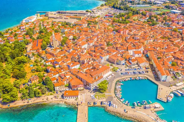 Slovenya 'nın Izola kentinin büyüleyici şehir merkezinin yukarıdan aşağı havadan görünüşü, dar Akdeniz sokaklarını ve Adriyatik kıyılarını dar ve renkli bir kıyı planıyla aydınlatıyor.