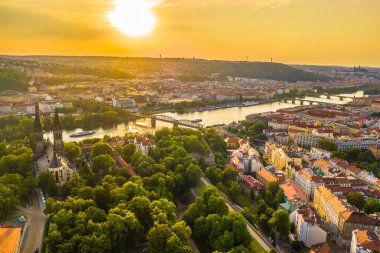 Çek Cumhuriyeti 'nin Prag kentinin üzerinde gün batımının havadan çekilmiş fotoğrafı, tarihi çatılar, Vltava Nehri ve yüzyıllar öncesinin mimarisi ile harmanlanan ılık tonların üzerine altın bir ışık tutuyor.