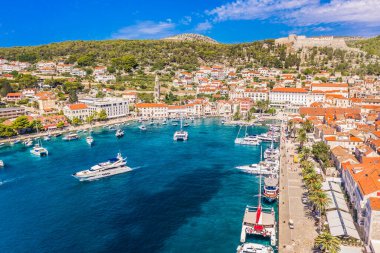 Hvar şehrinin insansız hava aracı fotoğrafı tam deniz kenarı, demirli tekneler, tarihi rıhtım, taş evler ve Adriyatik sularını yüksek perspektiften temizlerken güneş ışığıyla yıkandı.