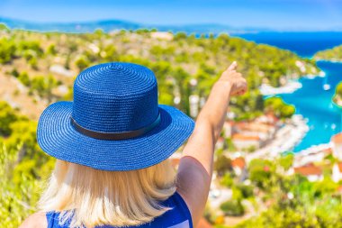 Arkadan görülen kadın turist Bobovisca na Moru 'nun üzerinde durarak turkuaz körfeze ve Akdeniz doğası ile çevrili pitoresk kıyı köyüne doğru bakıyor.