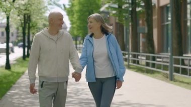 Sokakta yürürken el ele tutuşan olgun bir çift. Koşudan sonra dinlenen romantik aile manzarası. İnsanlar, spor, aşk ve iletişim konsepti