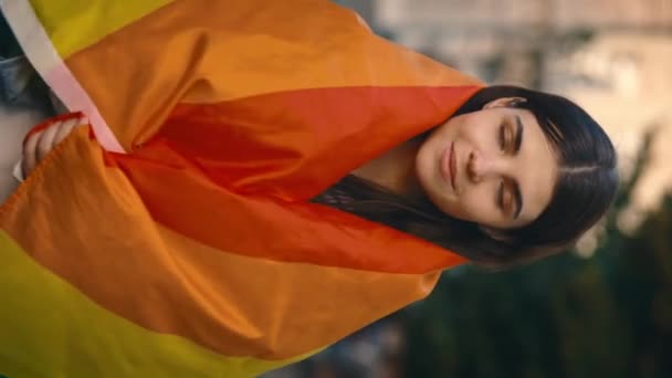 垂直ビデオ 垂直ビデオ カメラを向けると 若い女性がLgbtの旗に身を包んで微笑んだ姿が描かれている 街の通りに立つレズビアン女性 — ストック動画