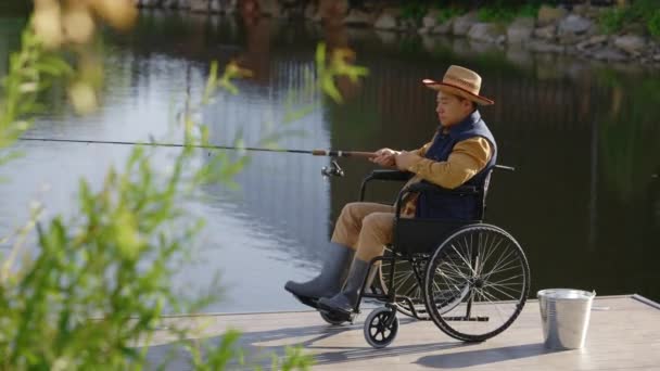 轮椅上的残疾渔民在码头的当地湖上钓鱼 他儿子给了他一个热水瓶和两杯热茶 人与关系 — 图库视频影像