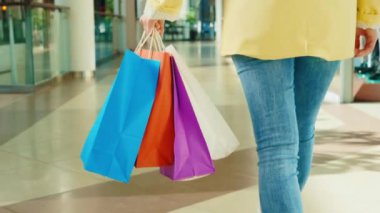 Alışveriş merkezine giden kadının yakından görüntüsü, elinde dükkandan gelen renkli kâğıt paketlerle. Alışverişten sonra kadın