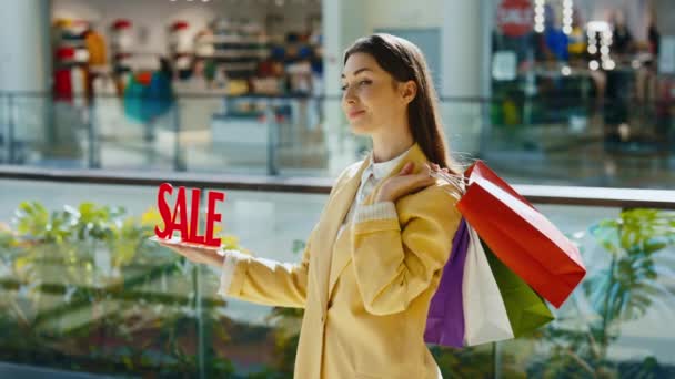 手里拿着红色销售标牌的女人的画像 提着许多彩色的包裹 购物后建议低价商品 — 图库视频影像