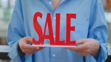 Mağaza indirimleri ve alışveriş. Kırmızı satış tabelasını tutan tezgahtarın elleri. Düşük fiyatlı mallar öneriliyor