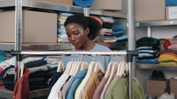 アフリカ系アメリカ人女性のボランティアは 古着や慈善団体で働いている間 リサイクルのための服でハンガーを越えていきます 再利用 意識した消費者 持続可能性の概念 — ストック動画
