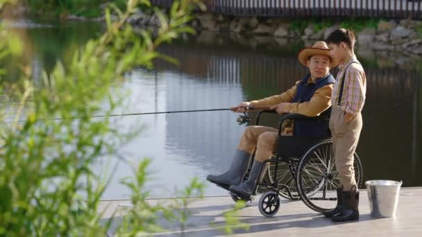 Niepełnosprawny Rybak Wózku Inwalidzkim Łowiący Ryby Miejscowym Jeziorze Molo Rozmawiający — Wideo stockowe