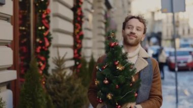 Gülümseyen adam Noel ağacı dükkanından evine gidiyor. Elinde küçük bir Noel ağacı var ve etrafa bakıyor. İnsanlar ve Noel tatili konsepti