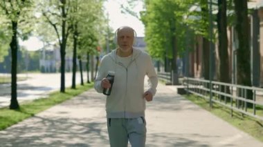 Gülümseyen mutlu yetişkin koşucunun portresi koşuyor ve arka planda spor şişesini tutuyor. Spor ve sağlıklı yaşam tarzı kavramı. Gençlik Yaşlanma