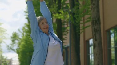 Müzik dinlerken egzersiz yapan olgun bir kadın. Kıdemli bayan koşucu geriliyor ve sokakta müzik dinliyor. Spor, yaşlılar ve sağlıklı yaşam tarzı konsepti