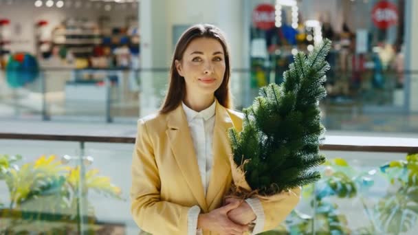 ポートレート女性の顧客は 新年のお祝いに準備を取得します 新しい年の店の後のバイヤー 笑顔の女性を保持していますクリスマスツリーショッピングモールに並んで — ストック動画