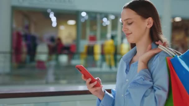 微笑的女顾客把她的购物放在商场里的纸袋里 女士拿着购物袋用她的智能手机女人购物后发短信 — 图库视频影像