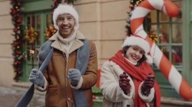 Mutlu çift ellerinde maytap tutarken süslü Xmas caddesinde keyifli bir şekilde dikiliyorlar. Kafkasyalı neşeli aile yeni yılı kutluyor. İnsanlar ve tatil kavramı