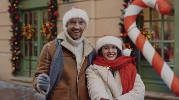 気分が良い装飾されたクリスマスストリートに立っている間 楽しいカップルは輝きを保持しています 新年を祝う白人の陽気な家族とカメラを見て 人と休日の概念 — ストック動画