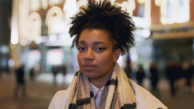 Gülümseyen Afrikalı Amerikalı kadın güzel bir gece sokağının ortasında kameraya bakıyor. Arka planda Noel tabelası var. Şenlik sezonu. Portre