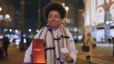 Afrika kökenli Amerikalı bir kadın elinde Noel kutusu ve kahveyle kış caddesinde yürüyor. Yeni yıl hazırlığı. Xmas