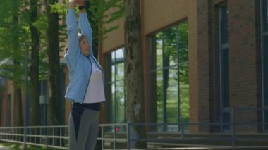 Müzik dinlerken egzersiz yapan olgun bir kadın. Kıdemli koşucu kadın yana eğiliyor ve sokakta müzik dinliyor. Spor ve sağlıklı yaşam tarzı kavramı. Gençlik Yaşlanma