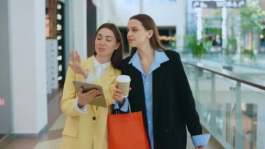 Kendi stilistiyle alışveriş merkezine dijital tablet kullanan bir kadın. Alışveriş merkezinde müşteri ve alışveriş asistanı birlikte.