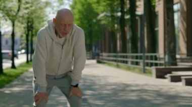 Yetişkin bir koşucu, sabah sokakta kulaklık takıp derin bir nefes almak için durur. Spor, eğlence ve sağlıklı yaşam tarzı konsepti. Gençlik Yaşlanma