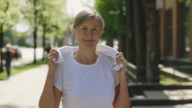 Eğitimden sonra sokakta kameraya bakan olgun koşucu kadının portresi boynunda bir havlu taşıyor. Spor ve sağlıklı yaşam tarzı kavramı. Gençlik Yaşlanma