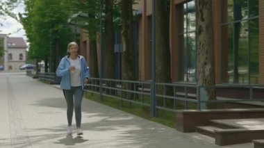 Happy gülümseyen olgun kadın koşucu koşuyor ve arka planda spor şişesini tutuyor. Spor ve sağlıklı yaşam tarzı kavramı