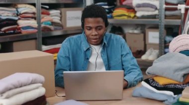 Kıyafet tasnif merkezinde dizüstü bilgisayarla çalışan çok ırklı erkek yönetici ya da bir sürü kıyafet kutusuyla bağış merkezi. İnsani yardım ve gönüllüler konsepti