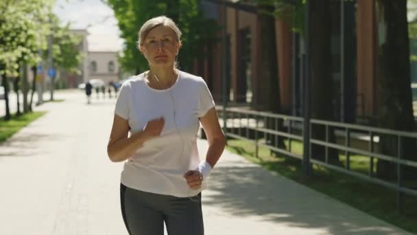 Olgun Gülümseyen Kadın Koşucu Kolunda Bandajla Caddede Koşup Müzik Dinliyor — Stok video