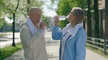Sokakta koştuktan sonra su içen olgun erkek ve kadın. Yaşlı çift dışarıda konuşuyor ve koşudan sonra su içiyorlar. Spor, iletişim, insanlar ve aşk konsepti