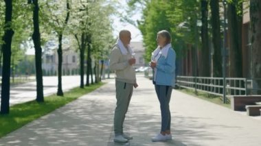 Koştuktan sonra konuşan olgun bir çift ellerinde su şişesiyle havluyu boyunlarında taşıyor. Spor, iletişim ve ilişki kavramı. Gençlik Yaşlanma