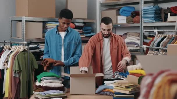 Two Male Volunteers Folding Clothes Putting Cupboard Box Warehouse Humanitarian — Vídeo de Stock