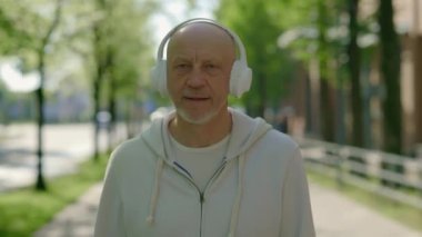 Kulaklık takıp kameraya bakan gülümseyen olgun adamın portresi. Sportif erkek sporcu koşmadan önce kameraya bakıyor. Spor ve sağlıklı yaşam tarzı kavramı