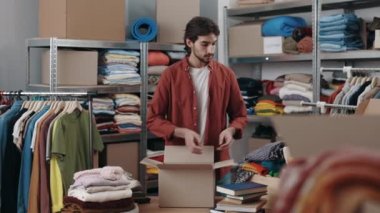 Çok kültürlü erkek gönüllü geri dönüşüm için kıyafet seçiyor ya da bağışlıyor ve yardım dükkanındaki dolaba koyuyor. Yeniden kullanım, ikinci el, bilinçli tüketici, sürdürülebilirlik kavramı