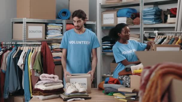 Young Caucasian Guy Volunteer Sorting Clothes Donation His Female Colleague — Stock Video