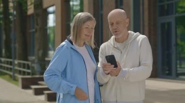 Son sınıf çifti eğitimden sonra sokakta duruyor ve akıllı telefonla müzik, podcast veya görüntülü sohbet dinliyor. Spor, teknoloji, iletişim ve sağlıklı yaşam tarzı kavramı