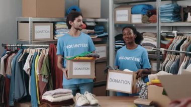Çeşitli gönüllülerin portresi. Dolapta giysileri olan kutular taşıyorlar ve kameraya gülümseyerek bakıyorlar. Arkasında eşyalar olan raflar. Bağış konsepti. Hayır Kurumu