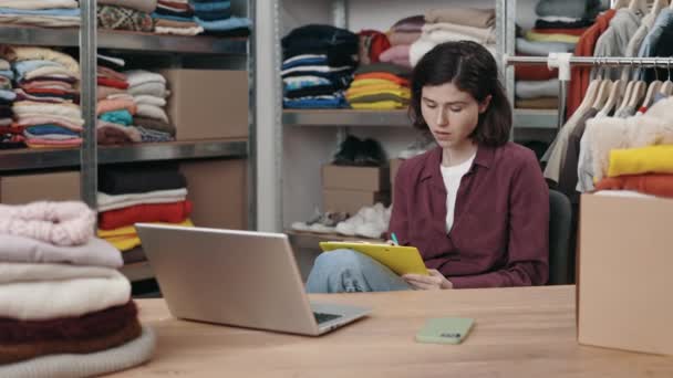 白种人女人坐在桌面上的笔记本电脑旁 一边工作一边做笔记 或者重复使用衣服中心 人道主义援助和可持续性概念 — 图库视频影像