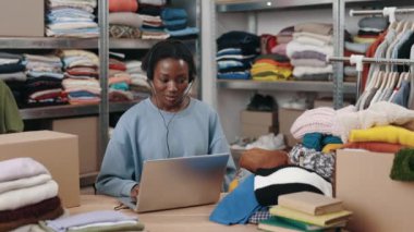 Çok ırklı engelli kadın yönetici kulaklıklı müşteriyle konuşuyor, giyim mağazasında dizüstü bilgisayarda çalışıyor. Küçük işletme, mağaza konsepti, girişimci