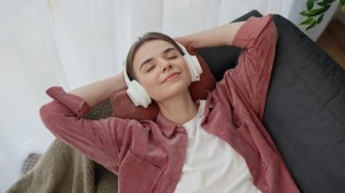 Güzel beyaz kadın kanepeye uzanmış, gözleri kapalı kulaklıkla müzik dinlemekten zevk alıyor. Evdeki insanlar. Üst görünüm