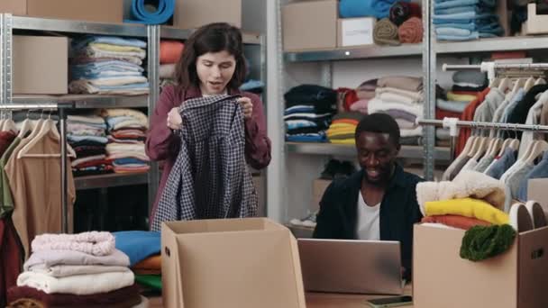 白人女工把衣服折叠起来 放进靠近男同事的再利用中心的橱柜里 带着手提电脑 人道主义援助和二手概念 — 图库视频影像