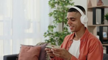 Kulaklık takmış, akıllı telefonda video oyunu oynayan Afro-Amerikalı bir adam. Oturma odasında kanepede oturan ve telefonda oyun oynayan genç adam. Teknoloji ve iletişim konsepti