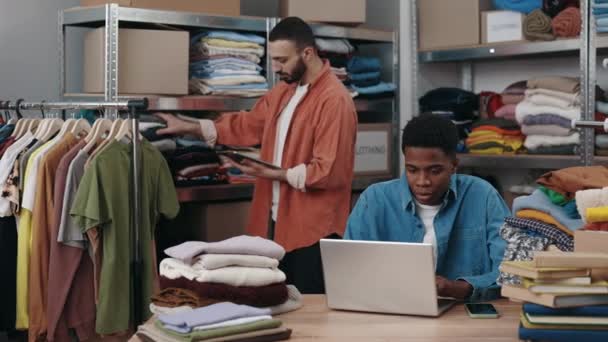 Mannelijke Vrijwilliger Typt Laptop Terwijl Zijn Blanke Collega Kleding Sorteert — Stockvideo