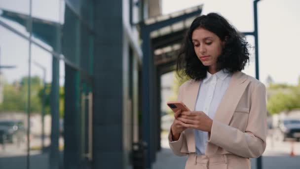穿着正装的漂亮的卷曲微笑的年轻女商人站在商务中心附近 用智能手机 人员和技术业务概念 — 图库视频影像