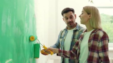 Beyaz bir aile dairede duvarları yeşil renkte boyuyor ve duvar fırçasıyla konuşuyor. Evde tamirat yapan çiftin yan görüntüsü. Sevgili çift dekorasyon odasını birlikte dekore ediyoruz.