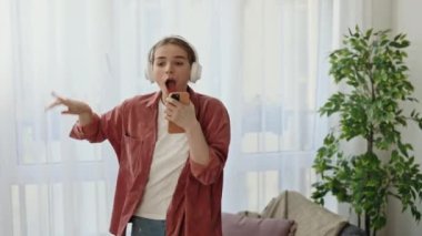 Telefondaki kulaklıkla müzik dinlerken dans eden ve şarkı söyleyen çılgın mutlu beyaz kadın. Teknoloji ve insanlar kavramı
