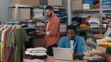 Giyim mağazasında çalışan çok ırklı insanlar müşteriye sevkiyat için siparişleri topluyor. Müşteri ile iletişim sırasında erkek yönetici dizüstü bilgisayar kullanıyor. Küçük işletme, evdeki uzak girişim