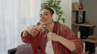 Telefondaki kulaklıkla müzik dinlerken dans eden ve şarkı söyleyen çılgın mutlu beyaz kadının portresi. Teknoloji ve insanlar kavramı