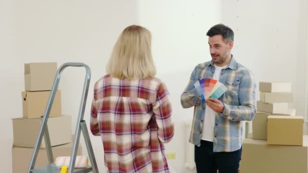 夫は彼の妻が新しい家の壁を描くための色を選択するのを助ける 男性労働者の腕時計を保持し 彼らはアパートで壁の色を議論 — ストック動画